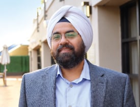 Amandeep Saluja smiling outdoors in a turban, glasses, and gray blazer.
