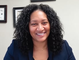 Courtney Holness smiling in a navy blazer against an office background.