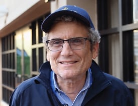 Daniel Vigilante smiling in glasses and a blue cap outdoors.