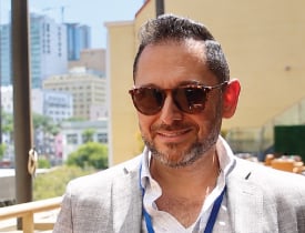 Edward Nisanov smiling in sunglasses and a light blazer by a window.