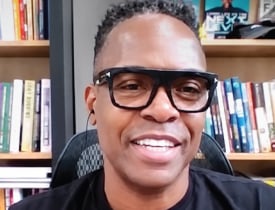 Jay Moore smiling in glasses in front of a bookshelf.