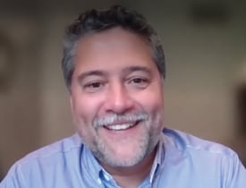 John Sanchez smiling in a light blue shirt against a softly blurred background.